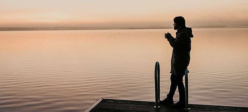 Mann auf einem Badesteg bei Sonnenaufgang