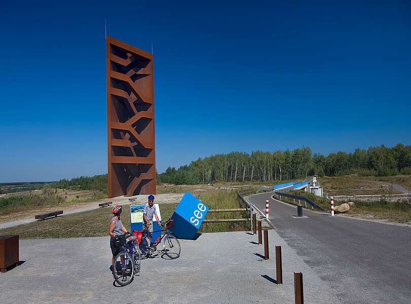 Radfahrer an der Landmarke Rostiger Nagel am Sedlitzer See
