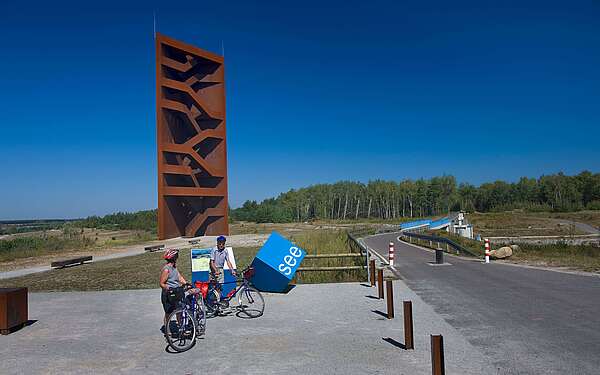 Radfahrer an der Landmarke Rostiger Nagel am Sedlitzer See