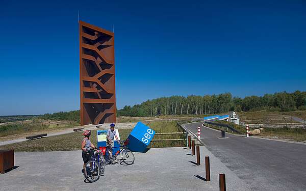 Radfahrer an der Landmarke Rostiger Nagel am Sedlitzer See
